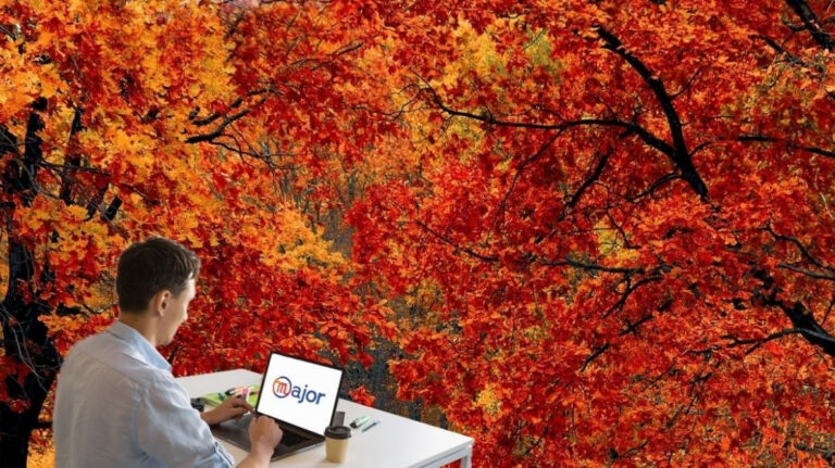 Un homme et son ordinateur devant des arbres avec des feuilles rouges et oranges