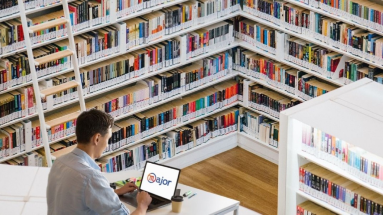 Un homme devant un ordinateur avec une bibliothèque derrière