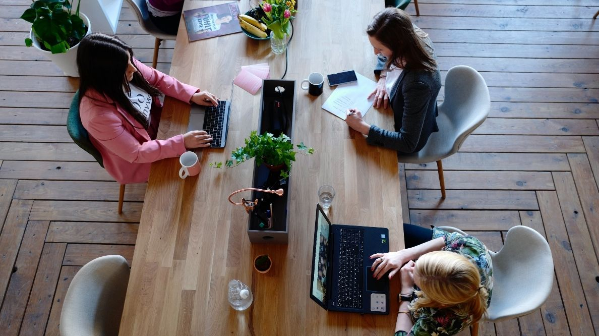 Trois femmes assises sur une chaise en face de la table devant un ordinateur/feuille