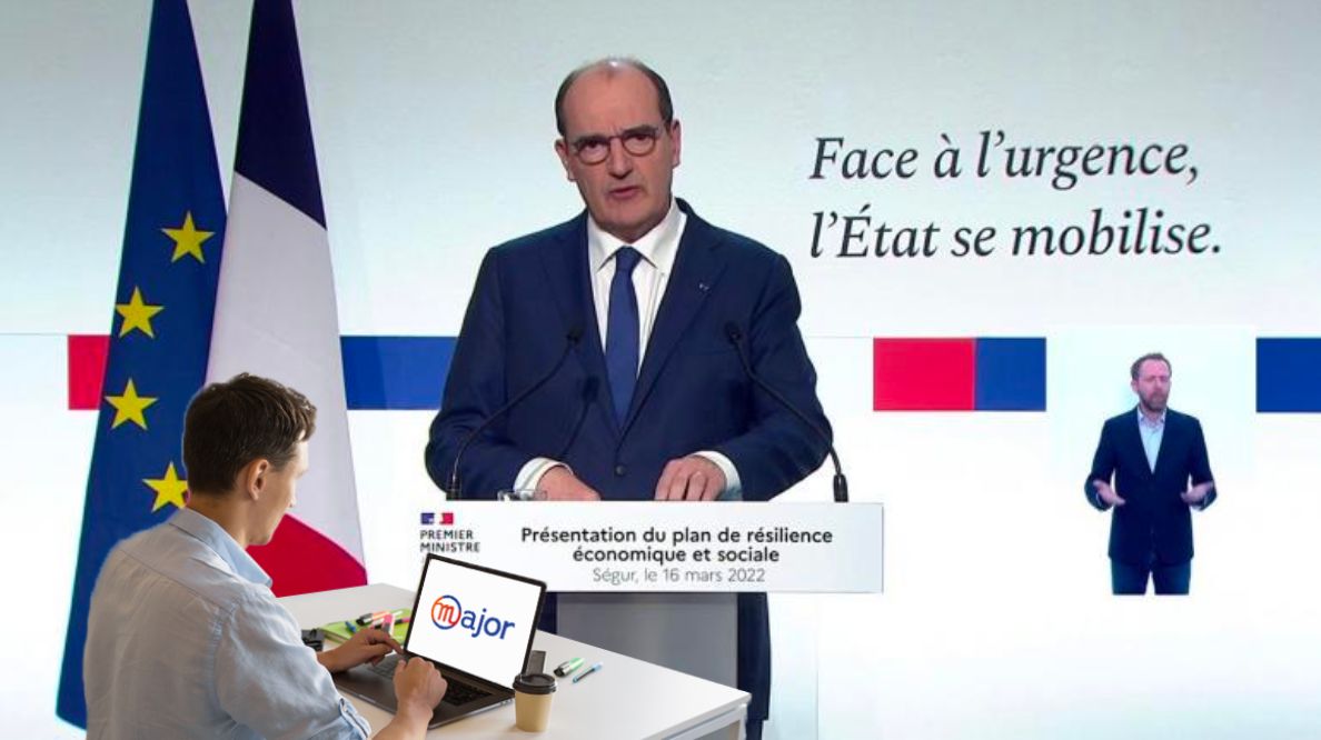 Un homme travaillant sur un ordinateur devant une conférence de Jean Castex