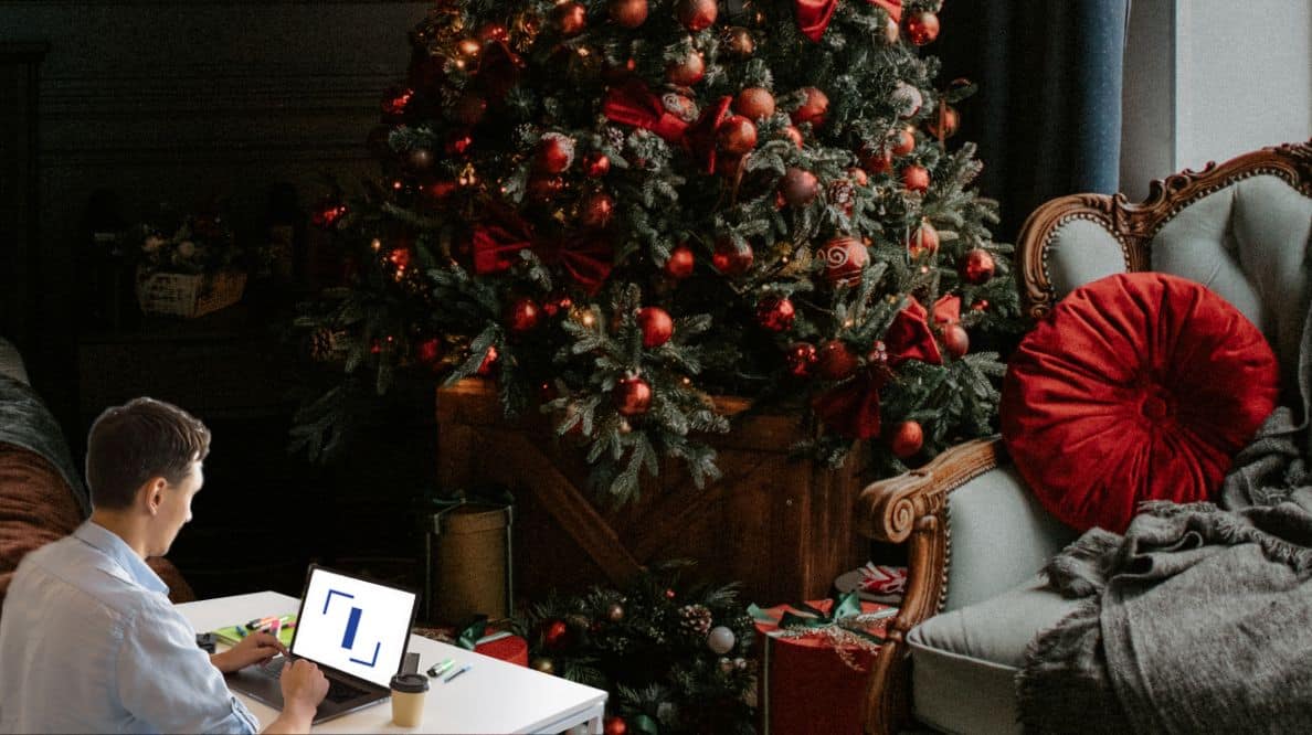 Un homme travaillant sur son ordinateur devant un sapin de Noël décoré