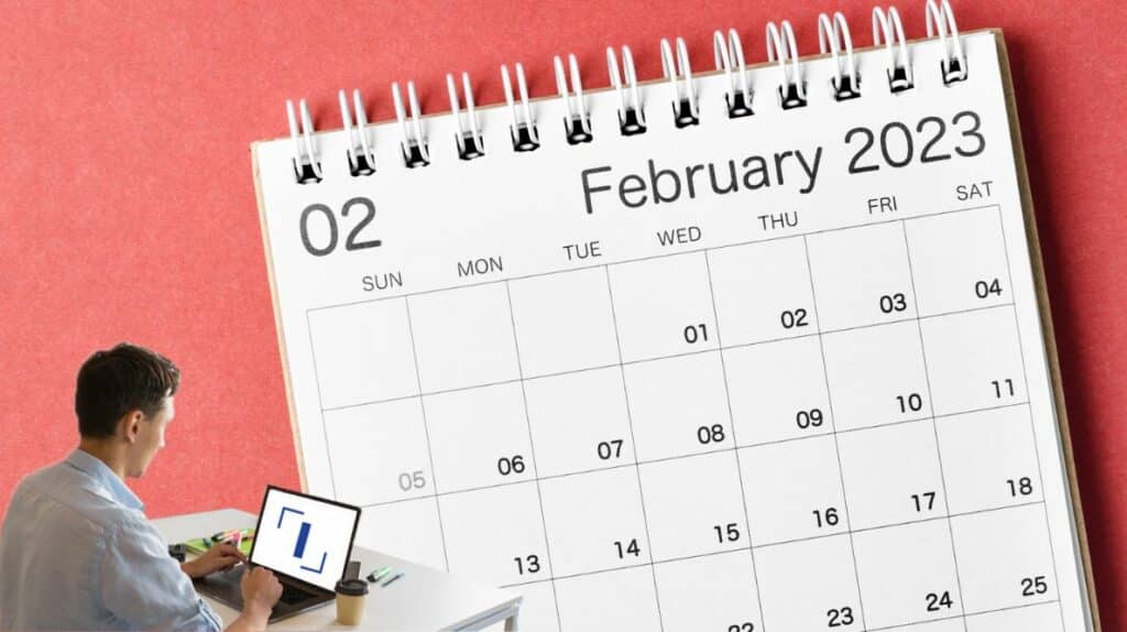 Un homme travaillant sur son ordinateur devant un planning du mois de février 2023