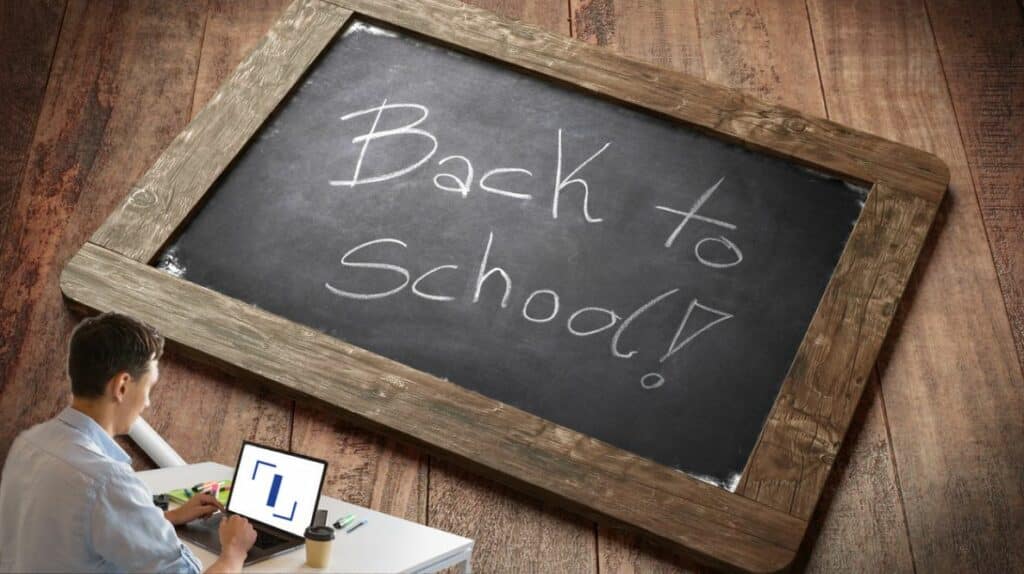 Un homme travaillant sur son ordinateur devant une ardoise sur laquelle il est écrit "back to school" ("retour à l'école" en français)