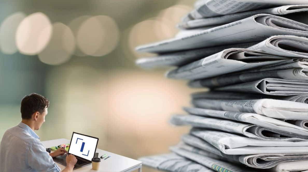 Un homme travaillant sur son ordinateur devant une pile de journaux