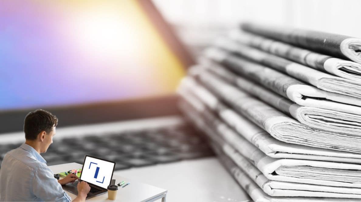 Un homme travaillant sur son ordinateur devant une pile de journaux.