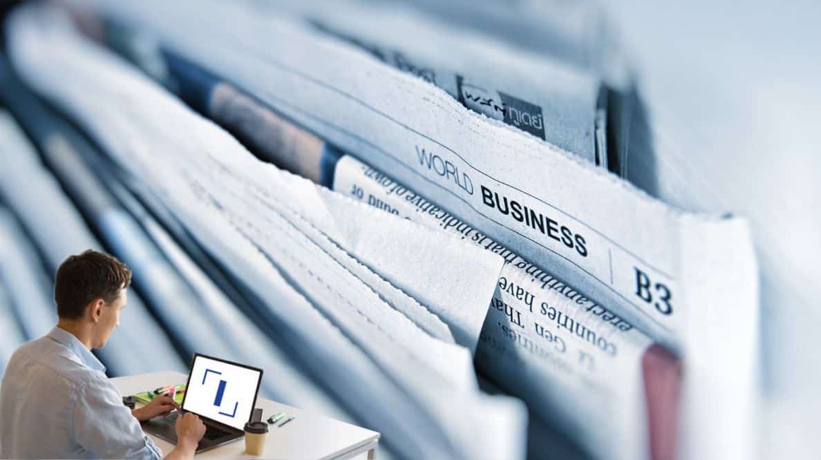 Un homme travaillant sur son ordinateur devant une pile de journaux